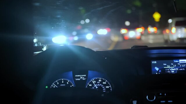 The driver's hand on the steering wheel of the night road and the glare of passing cars.