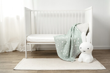 Baby wooden crib and toy rabbit in nursery room
