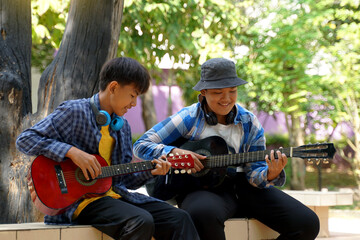 Two Asian boys were having fun playing classical guitar together during their free time at a school...