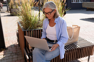 Fototapeta na wymiar mature woman with gray hair and glasses checks work cases using a laptop while on vacation