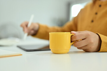 Cropped shot of woman hand holding cup of coffee and writing notes on digital tablet