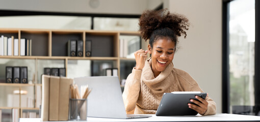 Smiling African black business woman using tablet while working on laptop at office. - obrazy, fototapety, plakaty