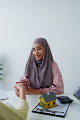 A female Muslim bank employee, holding hands, negotiates a residential loan with a customer.