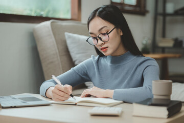 A student is sitting in the living room doing homework, Sitting and looking for information and making reports to send to teachers in the house, Recording various information In the book at apartment.