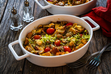 Bread casserole with mozzarella cheese, tomatoes and scrambled eggs on wooden table
