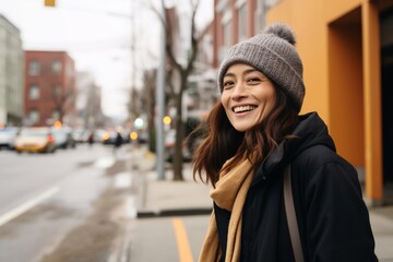Portrait of a smiling young asian woman in coat and hat standing on the street - obrazy, fototapety, plakaty