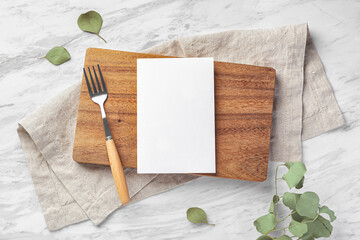Wooden board and menu card mockup with fork and linen napkin on marble kitchen table with green...