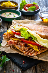 Big sandwich with grilled chicken breast and cheese and fresh vegetables on wooden table
