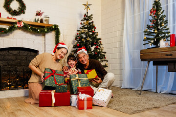 Obraz na płótnie Canvas Happy and cheerful Asian family gathering, wearing Santa hats talking and smiling. Exchanging gifts, grandparents and grandson daughter, sitting at the fireplace with decorated Christmas tree.