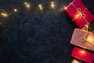 Christmas composition with gift boxes and lights of garland on black background. Empty copy space...
