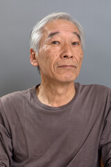 白髪混じりの60代の男性が、やや横向きながら目線はこちらに向けている。人の話を聞いているようにも見える。