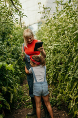 A mom with her tablet, her daughter hugging her tightly, and a backdrop of flourishing tomato plants