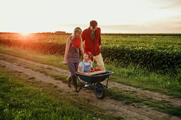 A happy family of three enjoys a beautiful sunset on their countryside farm after a hard day's work