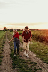 A joyful daughter runs to her beaming parents amidst the stunning countryside sunset, a perfect end to their day