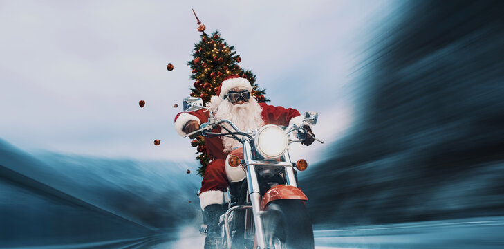 Contemporary Santa Claus riding a fast motorbike in the street and carrying a decorated Christmas tree