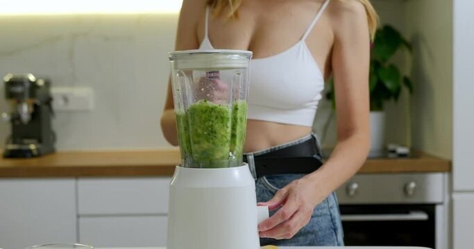 Woman is making green spinach and banana smoothie in blender. 
