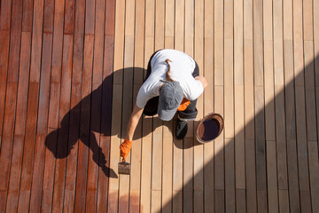 Coating with protective outdoor UV wood oil on the wooden surface of the lining boards, worker with paintbrush overhead view