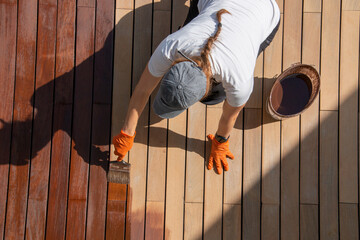 Workwoman staining wood deck boards outdoors, half body overhead view