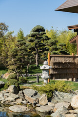 Fototapeta premium Japanese garden in Krasnodar Galitsky Park. Topiary art. Along shore of pond, between neatly trimmed trees and bushes, stands traditional Japanese stone lamp. Snow Lantern by Yukimi Toro.