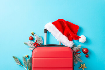 Santa's global journey lands at your event. A top view of a red suitcase, Santa's hat, pine boughs, mistletoe berries, festive decor, such as baubles and star on vivid blue backdrop with text space