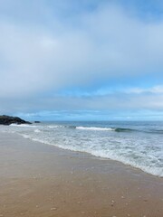 Waved ocean horizon, ocean coastline, sandy shore, splash and foam, cloudy sky, windy