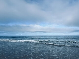 Fototapeta na wymiar Waved ocean horizon, ocean coastline, sandy shore, splash and foam, cloudy sky, windy