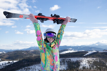 adult girl, a teenager, holds skis in her hands above her head, admires the mountain landscape and...