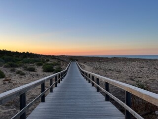 Fototapeta na wymiar Boardwalk to the ocean, orange horizon, blue pure sky, no people