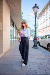 Full length of a blond haired woman using smartphone and walking on the city street