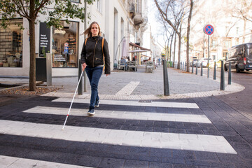 Visually impaired woman with white cane in hand walking through pedestrian crossing in the city