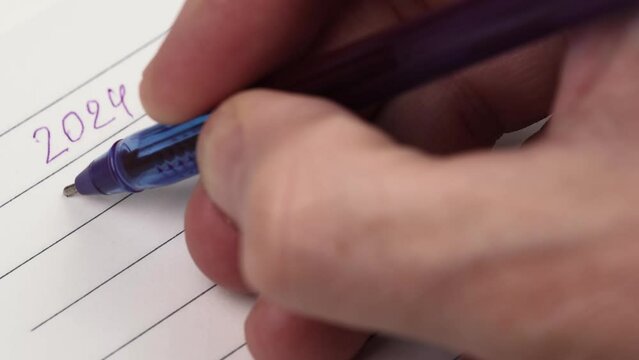 man's hand in a closeup notebook writes the numbers of the new year 2024 with a pen and emphasizes them. waiting for the holiday. thinking through and setting goals for the new year.