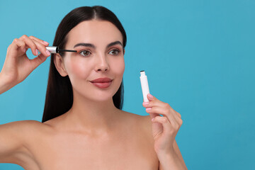 Obraz premium Beautiful woman applying serum onto her eyelashes on light blue background, space for text. Cosmetic product