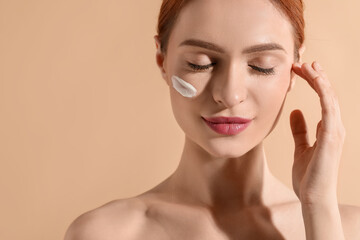 Beautiful young woman with sun protection cream on her face against beige background, space for text