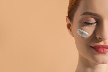 Beautiful young woman with sun protection cream on her face against beige background, closeup....