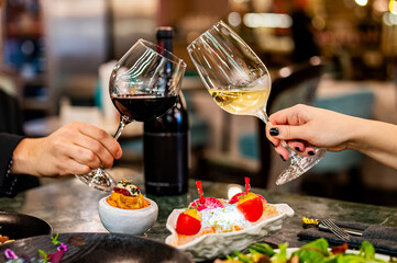 Close up of hands young couple man and woman clinking with glasses of red and white wine at restaurant