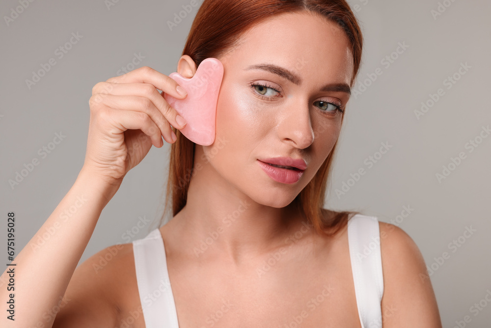 Canvas Prints Young woman massaging her face with rose quartz gua sha tool on grey background