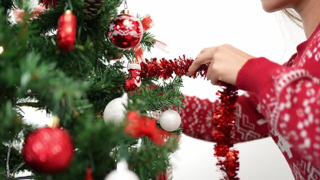 Merry christmas and happy holidays, hand of an asian woman is decorating the spruce tree with a tinsel garland, indoors home at winter. Xmas ball hanging of fir branches for decoration