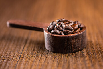 Roasted coffee beans in wooden scoop on wooden table.