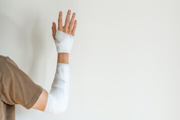 Young man with gauze bandage wrapped around his injured arm at home. Man with hand wrapped in medical bandage on white background. First aid, arm treatment after accident injury. Copy space