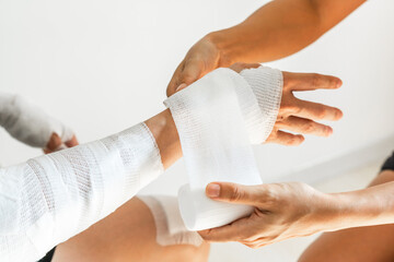 Sister wrapping her brother wrist and arm with bandage around injured hand over white background at home. First aid, accident and injury treatment concept. Closeup - obrazy, fototapety, plakaty