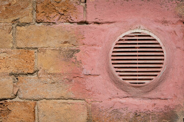 Il bocchettone di un impianto di aerazione su un muro di mattoni dipinto di rosa