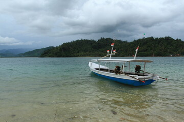 Fototapeta na wymiar Empty wooden boat with small Indonesian flags on top moorer on seaside.