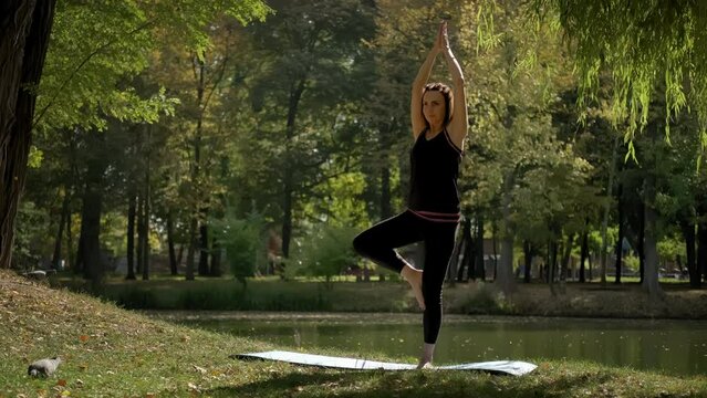 Wide view of Woman stand on yoga mat and practicing yoga stretching exercise outdoors in sunny day. slow motion footage