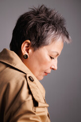 Profile of elegant mature woman in trench coat standing isolated on grey