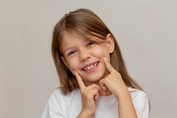 Portrait of caucasian happy little girl with open wide smile holding fingers on cheeks showing good...