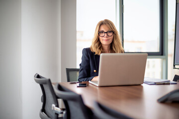 Mid aged businesswoman with notebook sitting at desk in a modern office and working