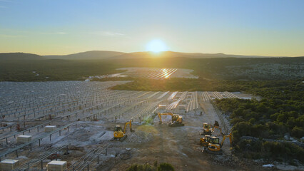 Aerial view over machinery at a solar farm construction site, during sunset