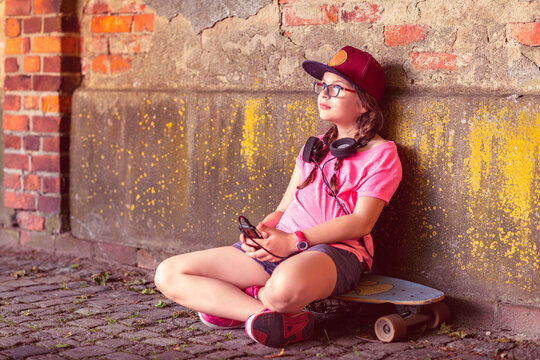 young beautiful hipster little girl sitting on skateboard in the city street