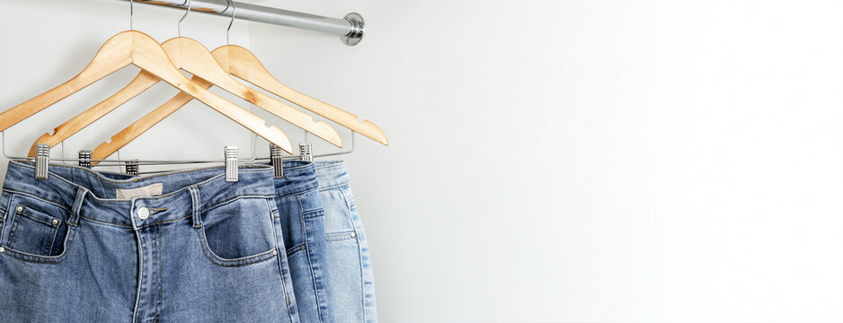 Close up jeans hang on wooden hangers in white dressing room. Wide banner. Place for text.