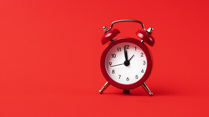 A classic red alarm clock stands out boldly against a monochromatic red background.